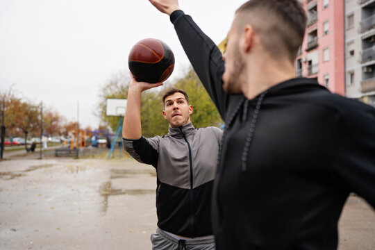 Athletic young man preparing to throw a ball over a defending opponent during a competitive streetball game in a residential neighborhood.