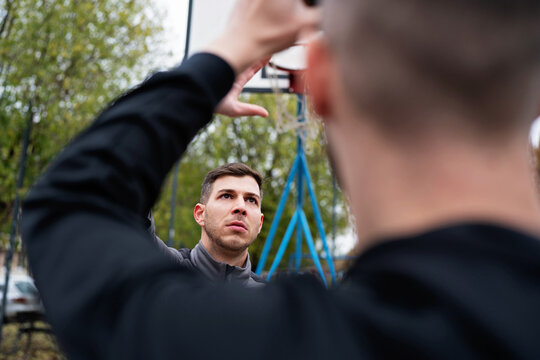 Two athletic men playing street basketball at an outdoor park, focusing on the game and basketball hoop.