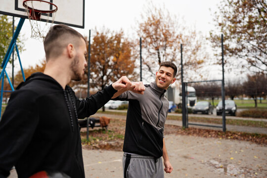 Athletic male friends sharing a moment of sportsmanship and camaraderie while training outdoors on an autumn urban basketball court.