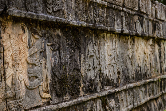 Close up perspective of weathered stone carvings and reliefs on the Tzompantli temple wall in Chichen Itza, Mexico