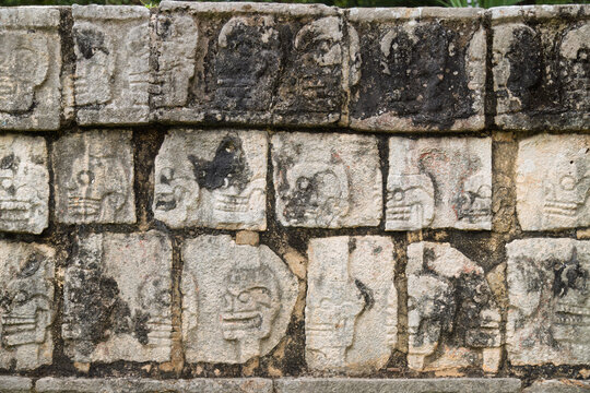 Close up of the weathered stone skull carvings arranged in rows on the Tzompantli wall in Chichen Itza, Mexico
