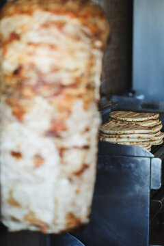 Rotisserie meat cooks beside a tall stack of soft pita bread in a Greek kitchen, ready to be sliced and wrapped into flavorful gyro, highlighting Mediterranean street food and casual dining.