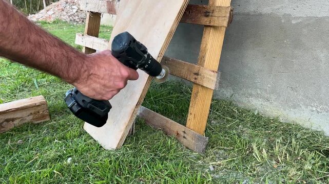 Worker hands using a cordless power drill with a wire brush attachment to sand and finish a rustic wooden board