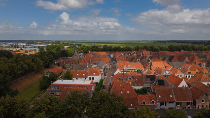 Obraz premium Horizontal photo of a picturesque old street in the historic fortified city of Elburg, Netherlands, featuring typical orange brick Dutch houses under a blue sky.