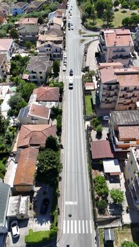 Vertical aerial drone view of long straight asphalt road with pedestrian crosswalk and driving cars between residential houses in Roseto degli Abruzzi Italy.