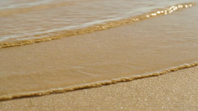 Ocean wave washing over sandy beach surface. Seawater rolling across wet golden sand. Tropical coastline tide retreat, nature background for summer vacation theme.