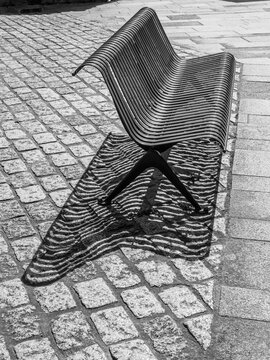 moderne Parkbank in einer Fu&szlig;g&auml;ngerzone wirft Schatten in Wellenform