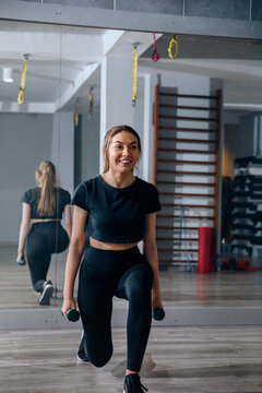 Woman performs lunges with dumbbells in gym during workout session