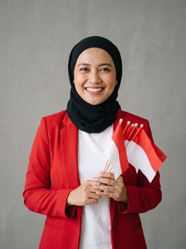Indonesian woman in hijab holding flags against grey background sharp focus portrait for national day marketing