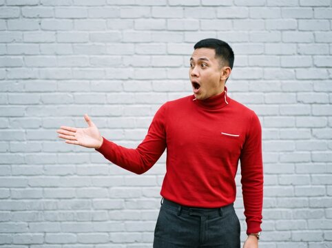 Shocked man gesturing sideways against white brick wall with sharp focus for marketing and sales advertising