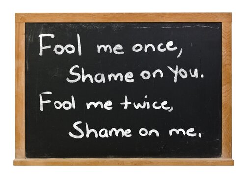 Fool me once shame on you written in white chalk on a black chalkboard in a wooden frame isolated on white