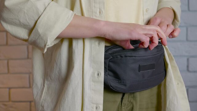 Person counting different currencies from a fanny pack. Close-up of female hands taking out, counting, and putting back various currencies like us dollars, euros from a black waist bag