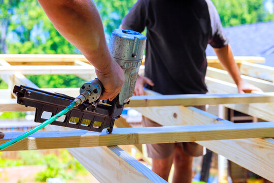 Construction workers use air nail gun to secure wooden beams in an outdoor setting