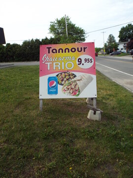 Gatineau,Quebec, Canada &ndash; May June 2, 2026:  A standalone sign advertising a "Tannour shawarma trio" for nine ninety-five stands roadside along Rue Belmont.