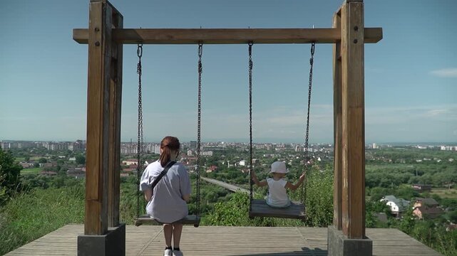 Tourist spot, swing with panoramic view, two girls riding, slow motion, sunny summer day