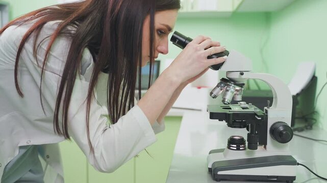 Lab worker woman looks in microscope.