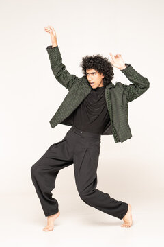 Young man with curly afro hair, intense gaze and bright white smile, wearing textured green quilted jacket, dynamic fashion pose in studio on white background