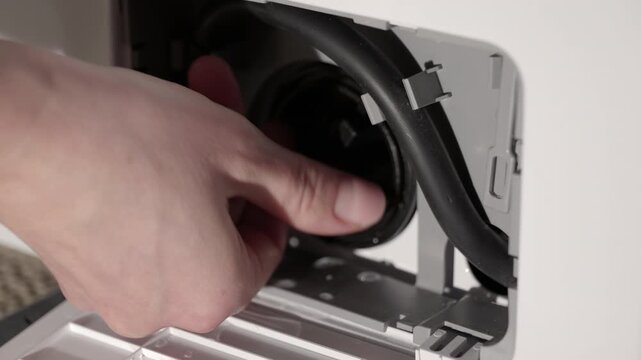 Person cleaning washing machine drain pump filter. Caucasian hand unscrewing and removing a drain pump filter from a household washing machine for cleaning and maintenance, preventing clogs
