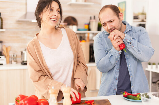 Man singing on red pepper in kitchen making wife smile, Girlfriend preparing salad, connecting sang on red pepper, in a home kitchen routine.