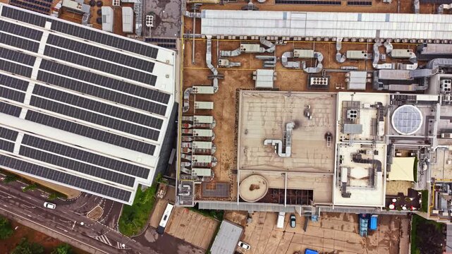 The scene shows a wide view of an industrial complex featuring solar panels on the roof. Several large air conditioning units are visible along with other equipment on the ground.