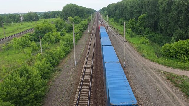 Elevated perspective of a freight train transporting shipping containers along a railway track, moving through a verdant forested area in the countryside
