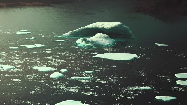 Icebergs of different shapes are visible in dark water. The sun reflects off the surface, creating patterns. The setting shows a remote area where these ice formations exist.