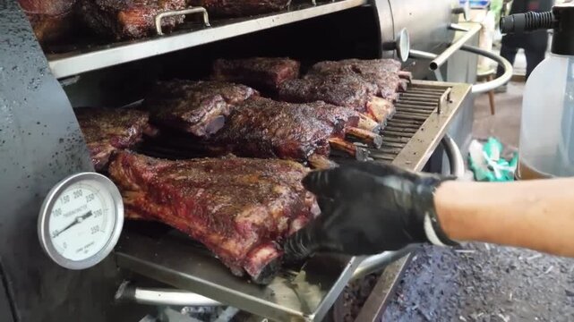 A close-up shot of a pitmaster opening a professional-grade barbecue smoker, showcasing succulent, tender beef ribs with a rich, caramelized crust cooking low and slow. The footage highlights the auth