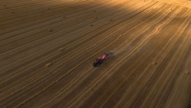 Aerial view of red square baler machinery baling straw on farmland with after good wheat harvest of successful farmer