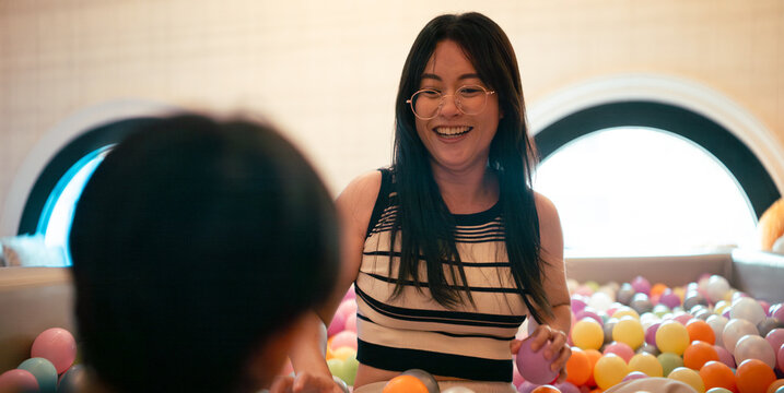Happy asian mom and toddler enjoying play time in a vibrant ball pool