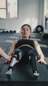 Young woman with prosthetic legs doing physical therapy exercise with trainer in gym interior