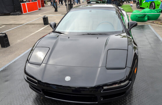 Pristine, glossy black Acura NSX sports coupe, capturing its iconic low slung wedge design, pop up headlight covers, and distinctive bright chrome wheels
