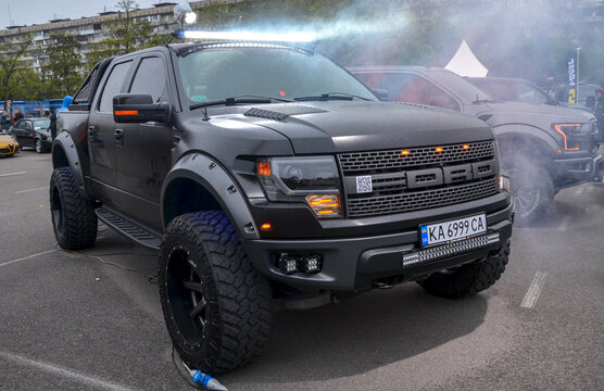 Rugged, matte black Ford F-150 SVT Raptor pickup truck features massive off-road tires, flared arches, and a bright roof LED light bar