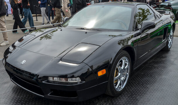 Pristine, glossy black Acura NSX sports coupe, capturing its iconic low slung wedge design, pop up headlight covers, and distinctive bright chrome wheels