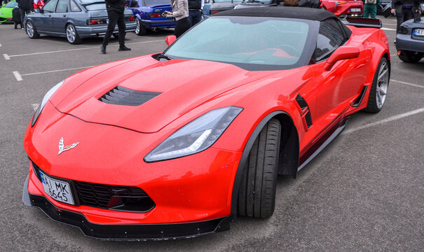 Striking red Chevrolet Corvette (C7) convertible, focusing entirely on its aggressive front fascia, crossed-flags emblem, vented hood, and sharp alloy wheels
