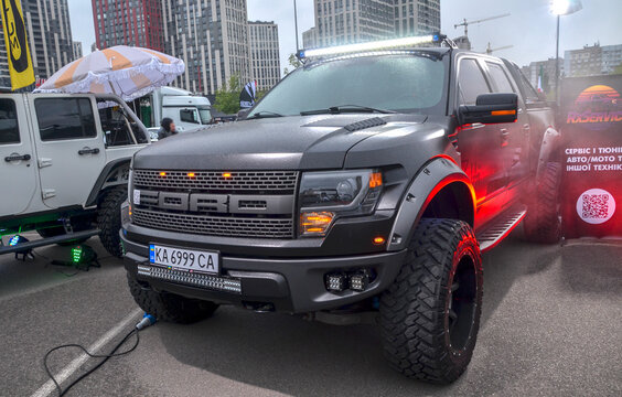 Rugged, matte black Ford F-150 SVT Raptor pickup truck features massive off-road tires, flared arches, and a bright roof LED light bar