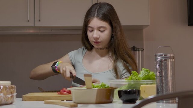 Smiling teenage girl enjoying her time in the kitchen while happily cutting fresh tomatoes on a wooden board to prepare a delicious and healthy vegetarian meal