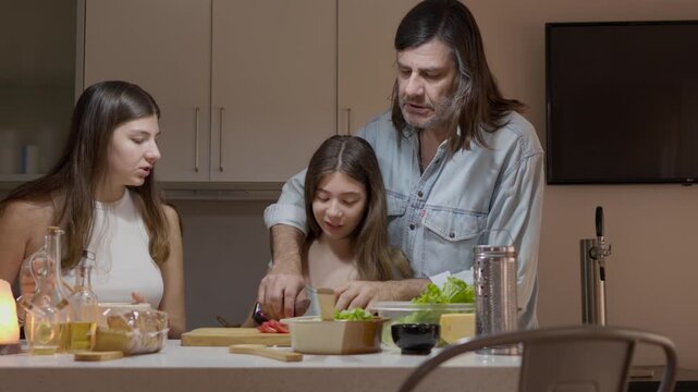A father enjoys a joyful cooking session with his two teenage daughters, preparing a healthy meal together. National Cooking Day