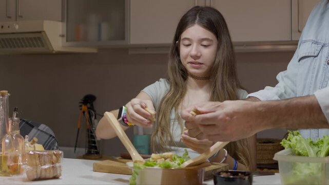 Father and teenage daughter preparing healthy salad together in modern kitchen, sharing laughter, teamwork and affection while cooking fresh vegetables at home