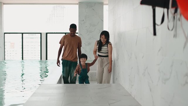 Mixed race family and son walking by an indoor swimming pool on vacation