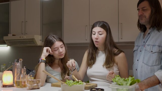 A modern family consisting of a single father and his two teenage daughters are preparing a meal together in their kitchen at home