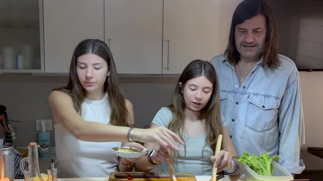 Single father enjoying an affectionate moment with his teenage daughters while cooking together at home