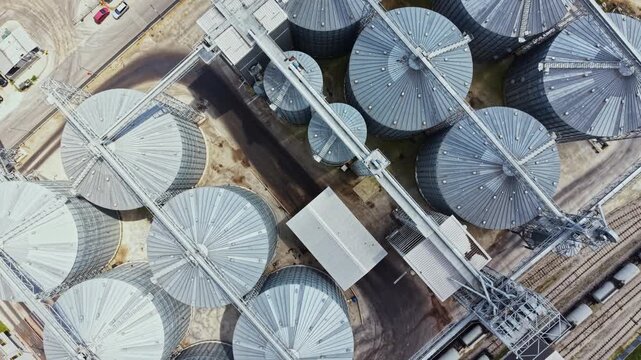 Above the ground, a collection of large metal silos stands in a farm setting. The silos are arranged in neat rows, with pathways connecting them.