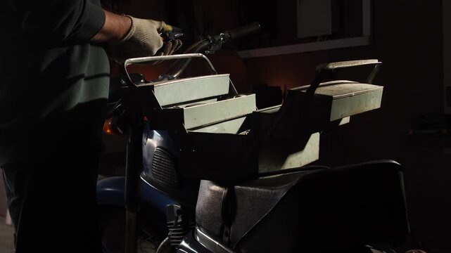 Person wearing gloves using a wrench, performing maintenance and restoration on a 1970s classic motorcycle next to an open toolbox in a dimly lit workshop