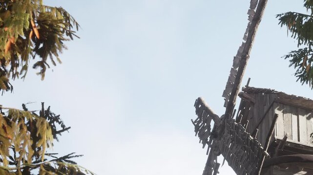 A wooden windmill stands tall with its blades turning slowly in the daylight. Surrounding trees provide a natural setting. The sky appears clear and bright above the structure.