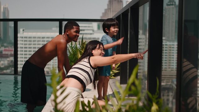 Mixed race family pointing at the city view from a rooftop pool