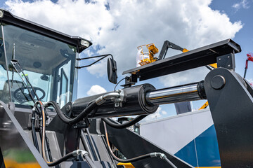 Wheel loader front boom lift hydraulic cylinder mechanism. Modern construction machinery section with chrome piston rod against sky background and technical engineering transport vehicle details. © NastyaPhoto