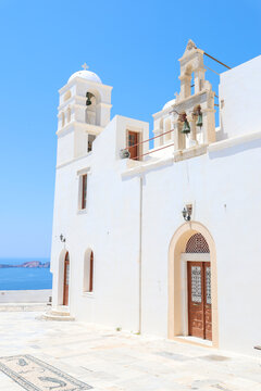 Whitewashed church with twin bell towers and arched doors overlooks the Aegean Sea under a vivid blue sky, capturing the luminous serenity and spiritual grace of Greek island architecture.
