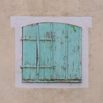 Faded mint‑green shutters framed in white against a beige wall reveal peeling paint and aged wood, showcasing the rustic charm and timeless texture of European architecture.