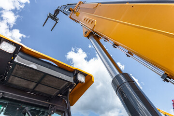 Telehandler telescopic boom arm raised above yellow cabin roof. Modern crane machinery mechanism with pallet forks attachment and heavy duty industrial transport vehicle technical details. © NastyaPhoto