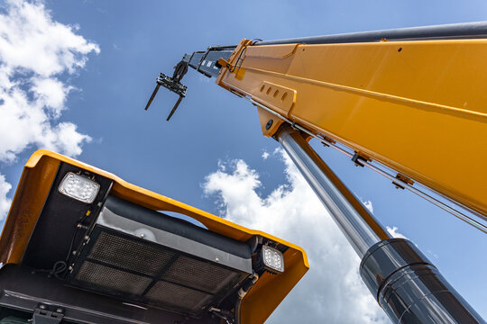 Telehandler telescopic boom arm raised above yellow cabin roof. Modern crane machinery mechanism with pallet forks attachment and heavy duty industrial transport vehicle technical details.